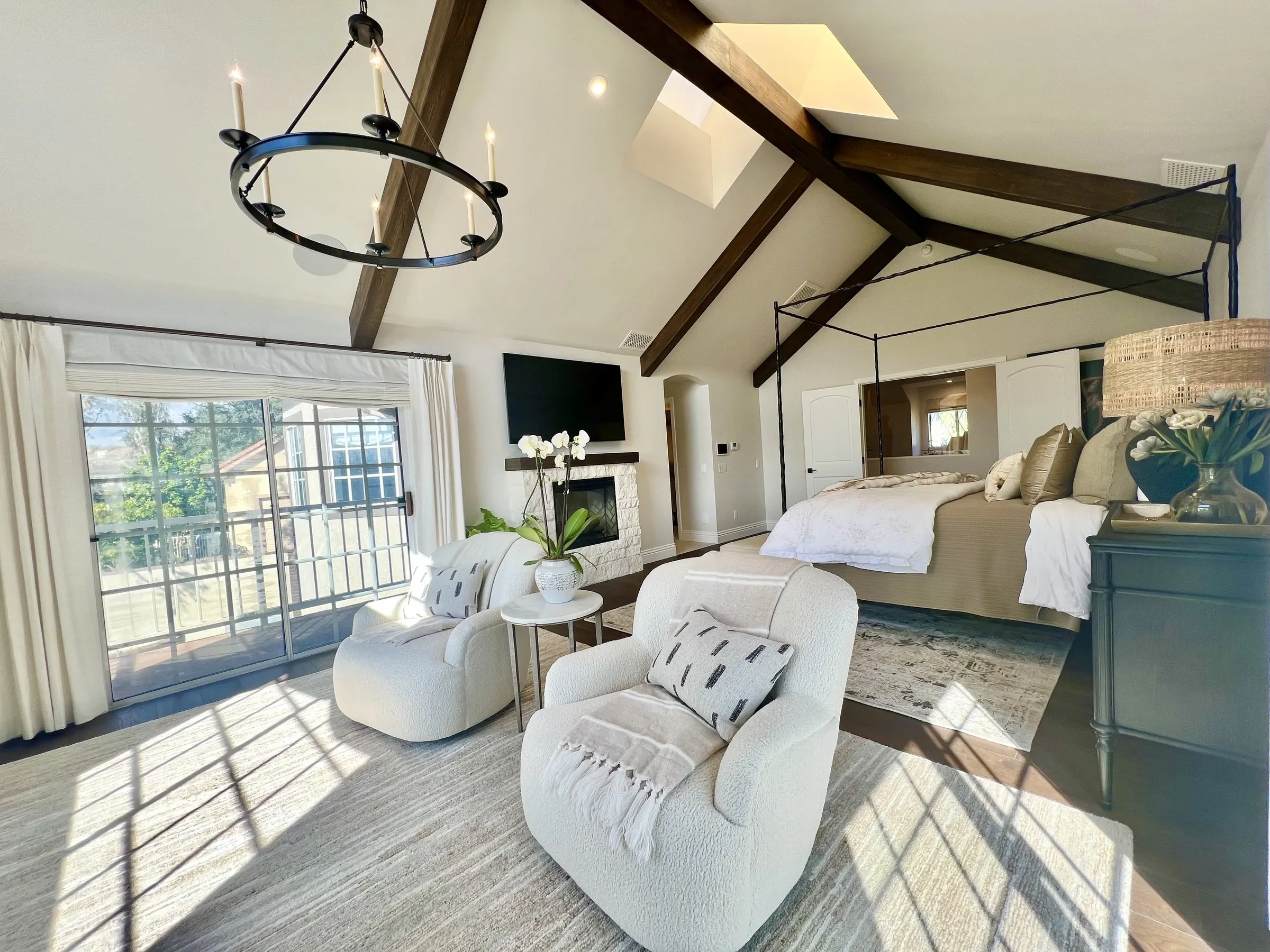 Bright primary bedroom with sunlight across the floor and a television above the fireplace
