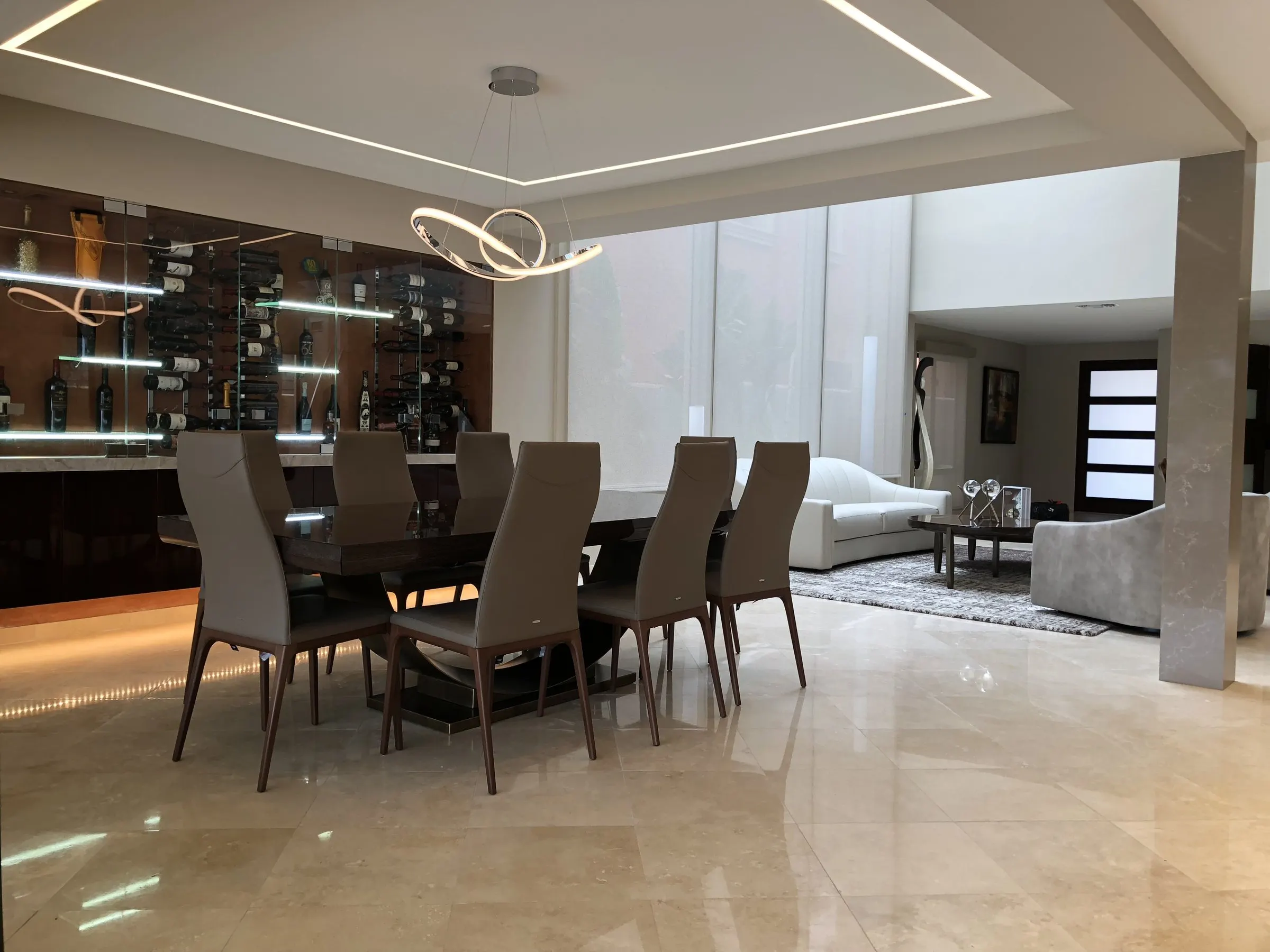Dining room with an LED ceiling cove, sculptural chandelier, and wine wall