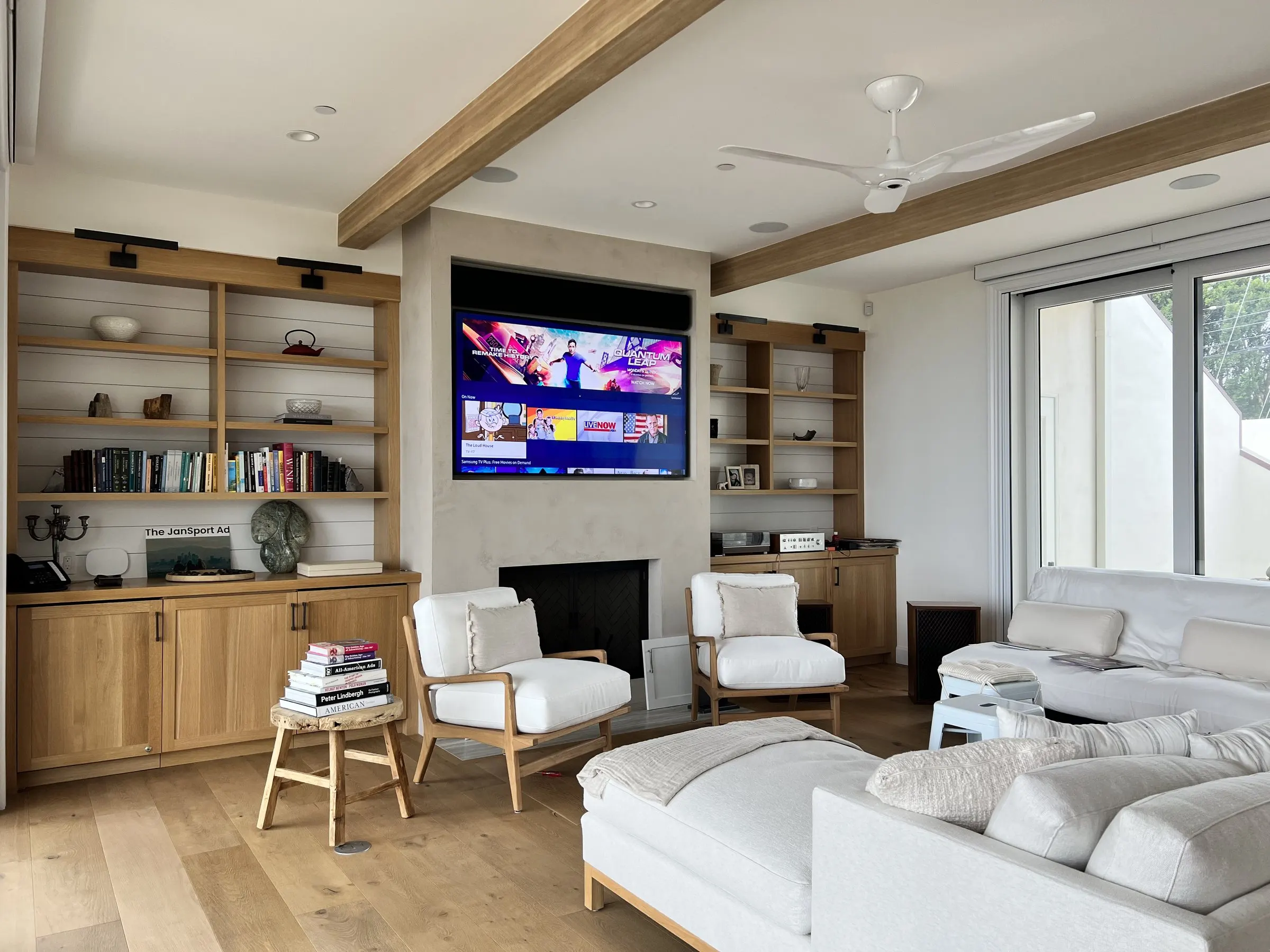 Family room with a television above the fireplace framed by oak shelving, white sofas in front
