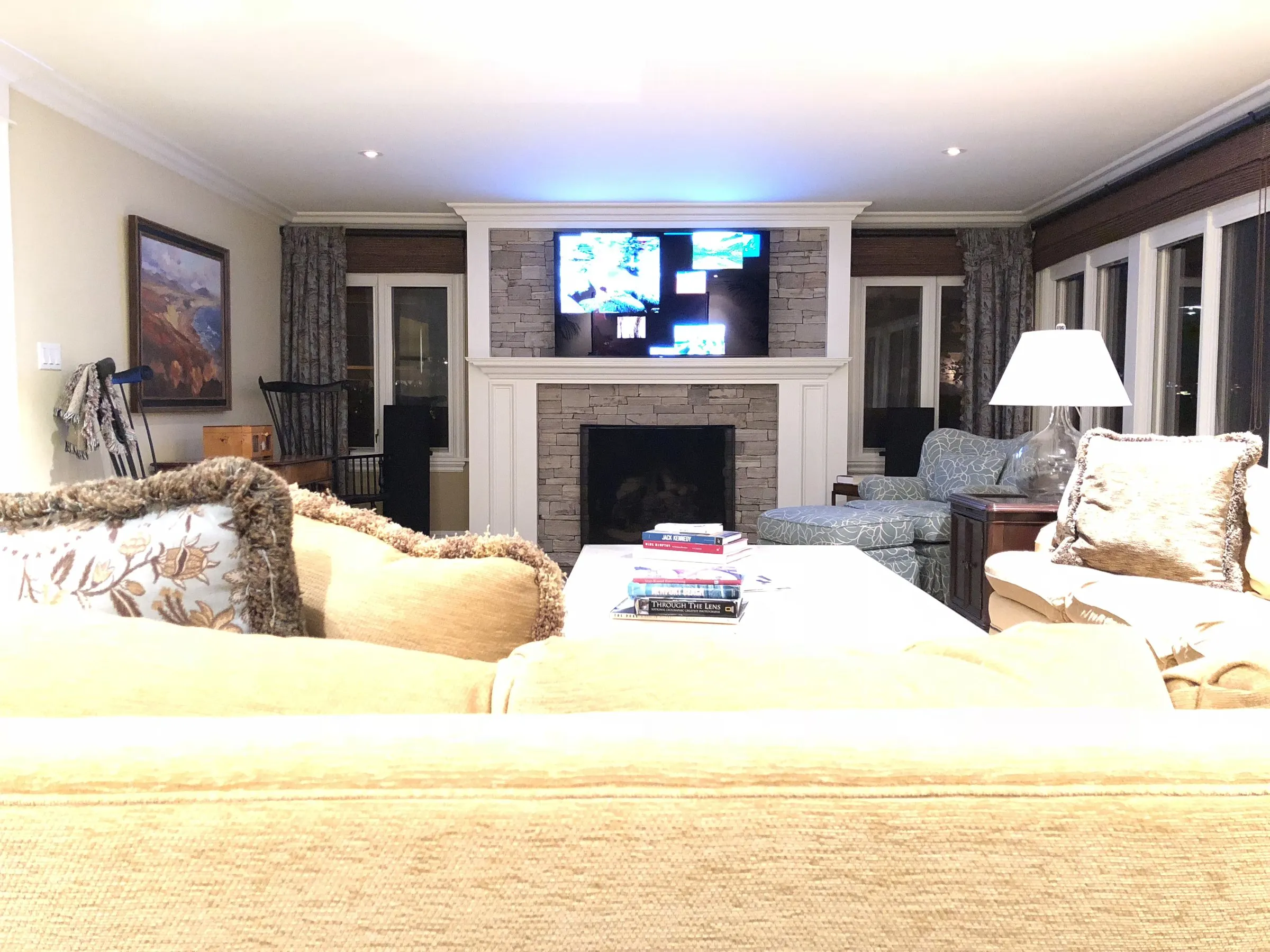Family room with a television above a stone fireplace and large windows