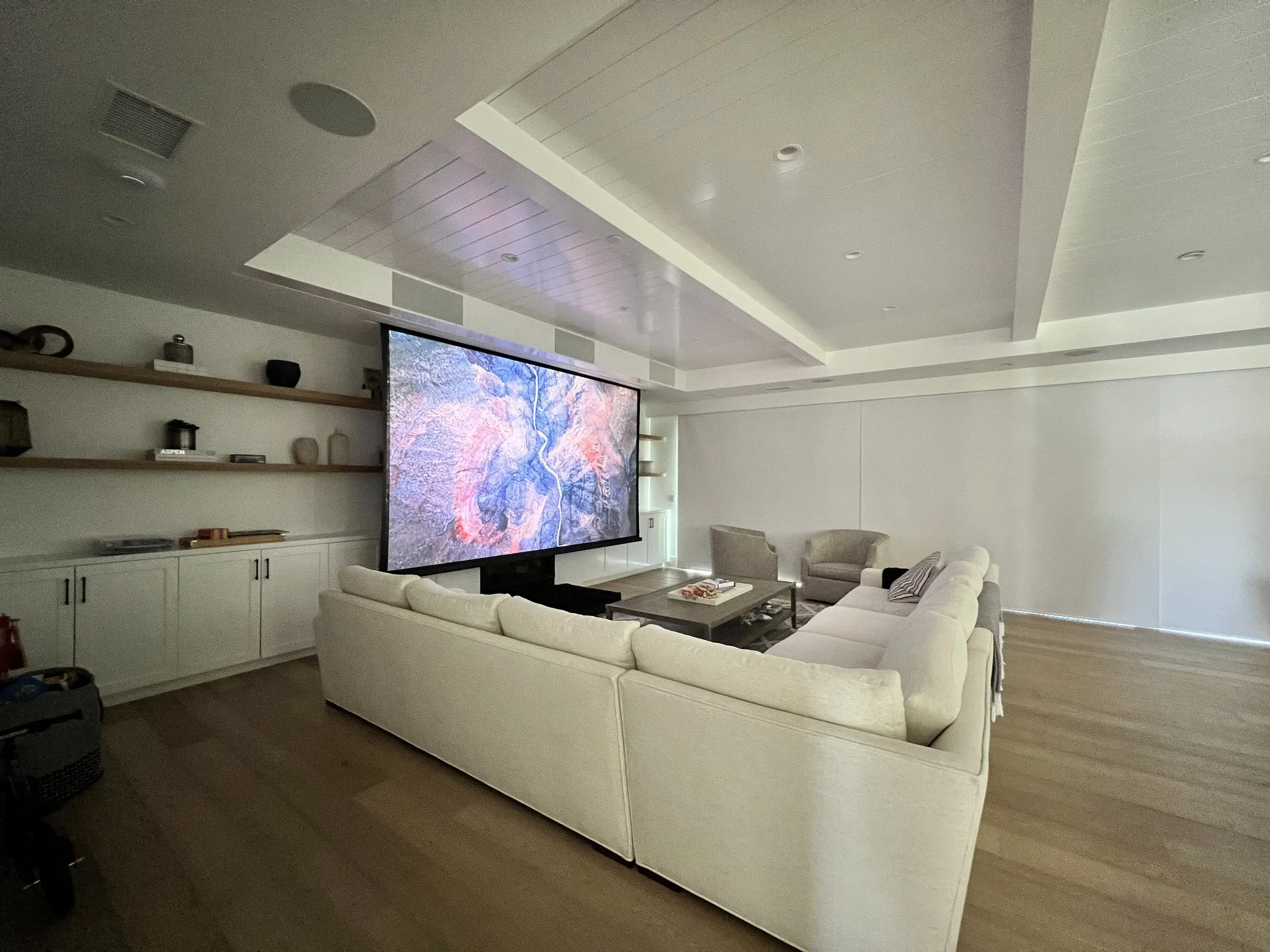 Family room with a sectional sofa and a large projection screen lowered in front of built-ins
