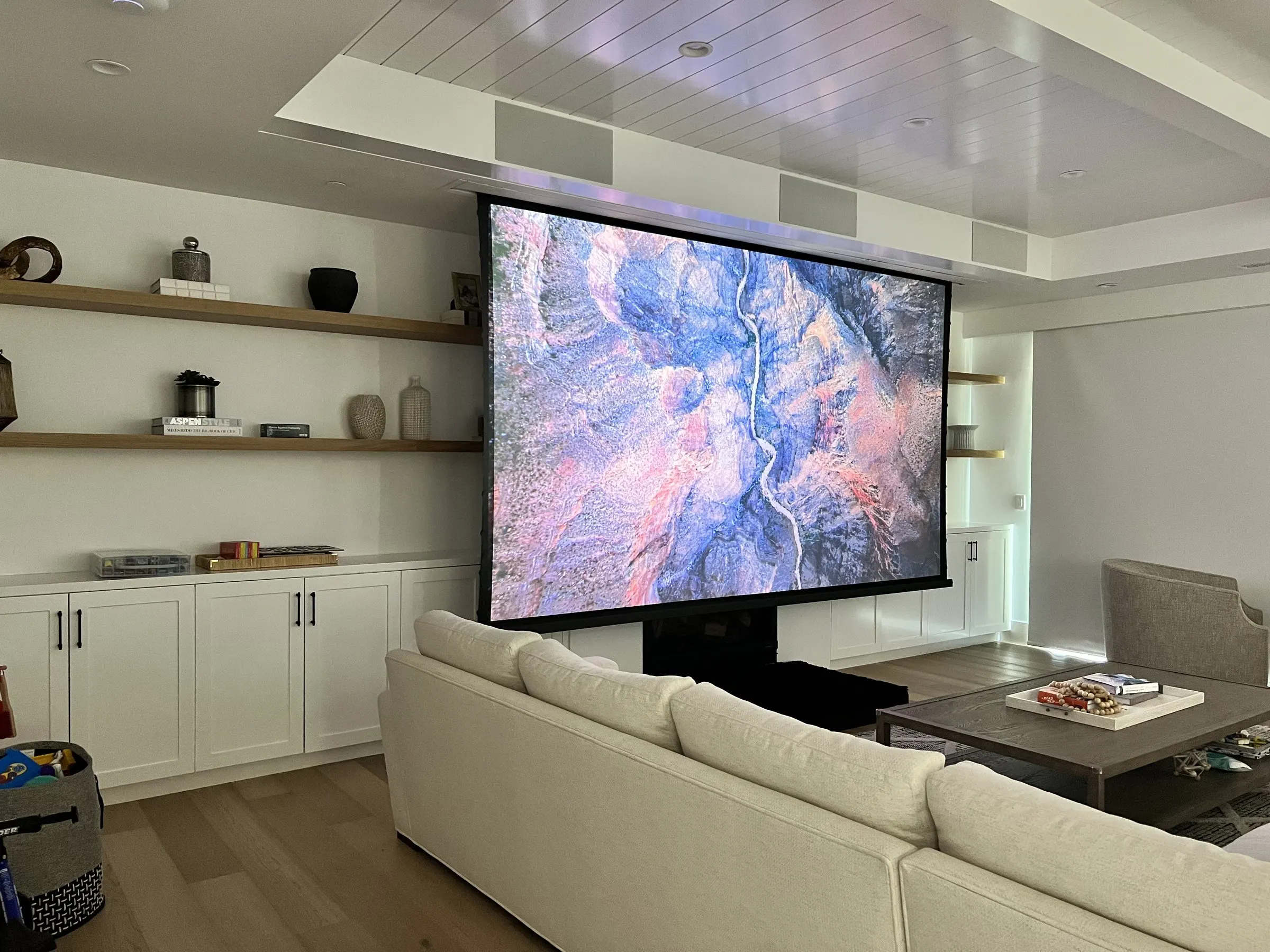 Family room with a large motorized screen lowered in front of built-in shelving, sectional sofa in front