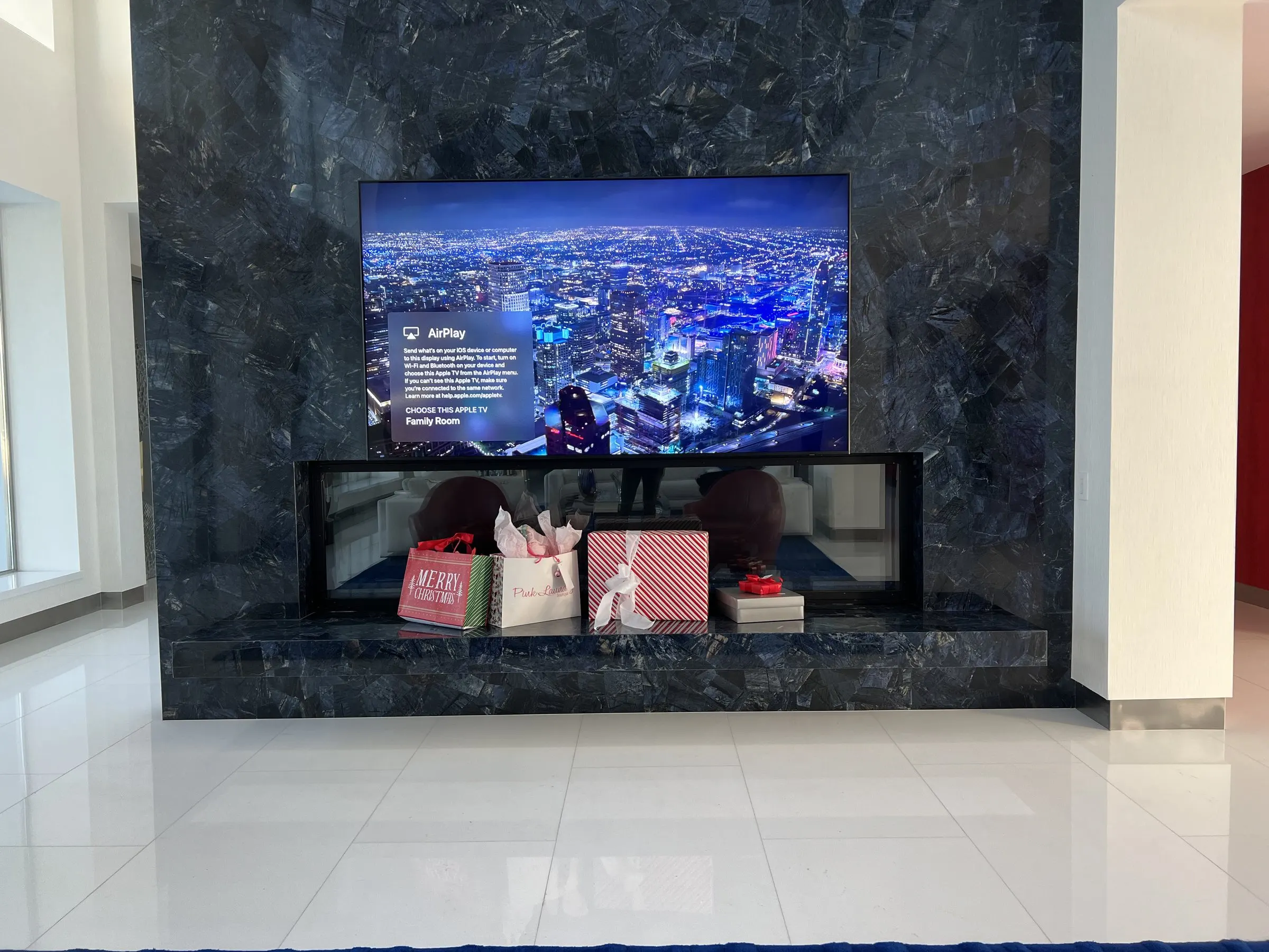 Television set into a blue stone fireplace wall above a linear fire