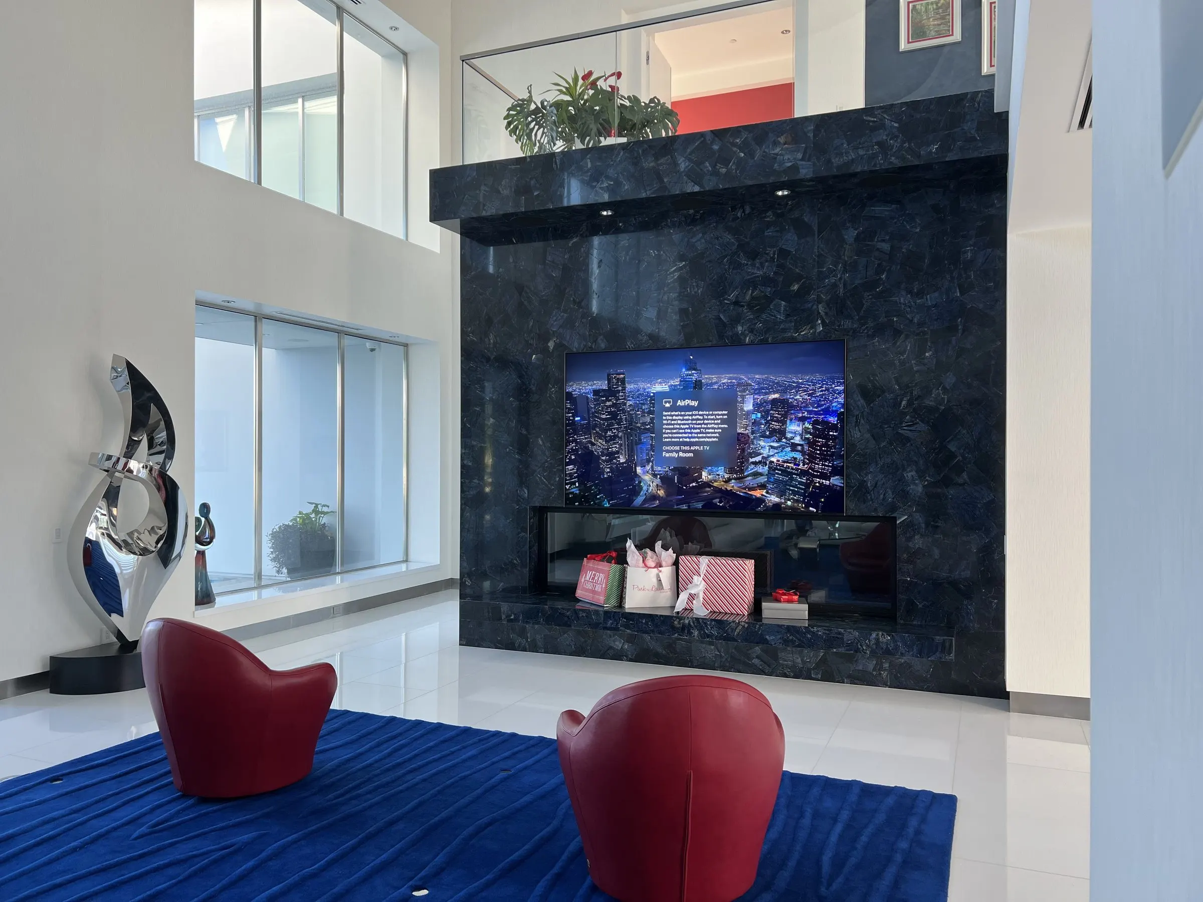 Television set into a dark stone fireplace surround in a double-height living room