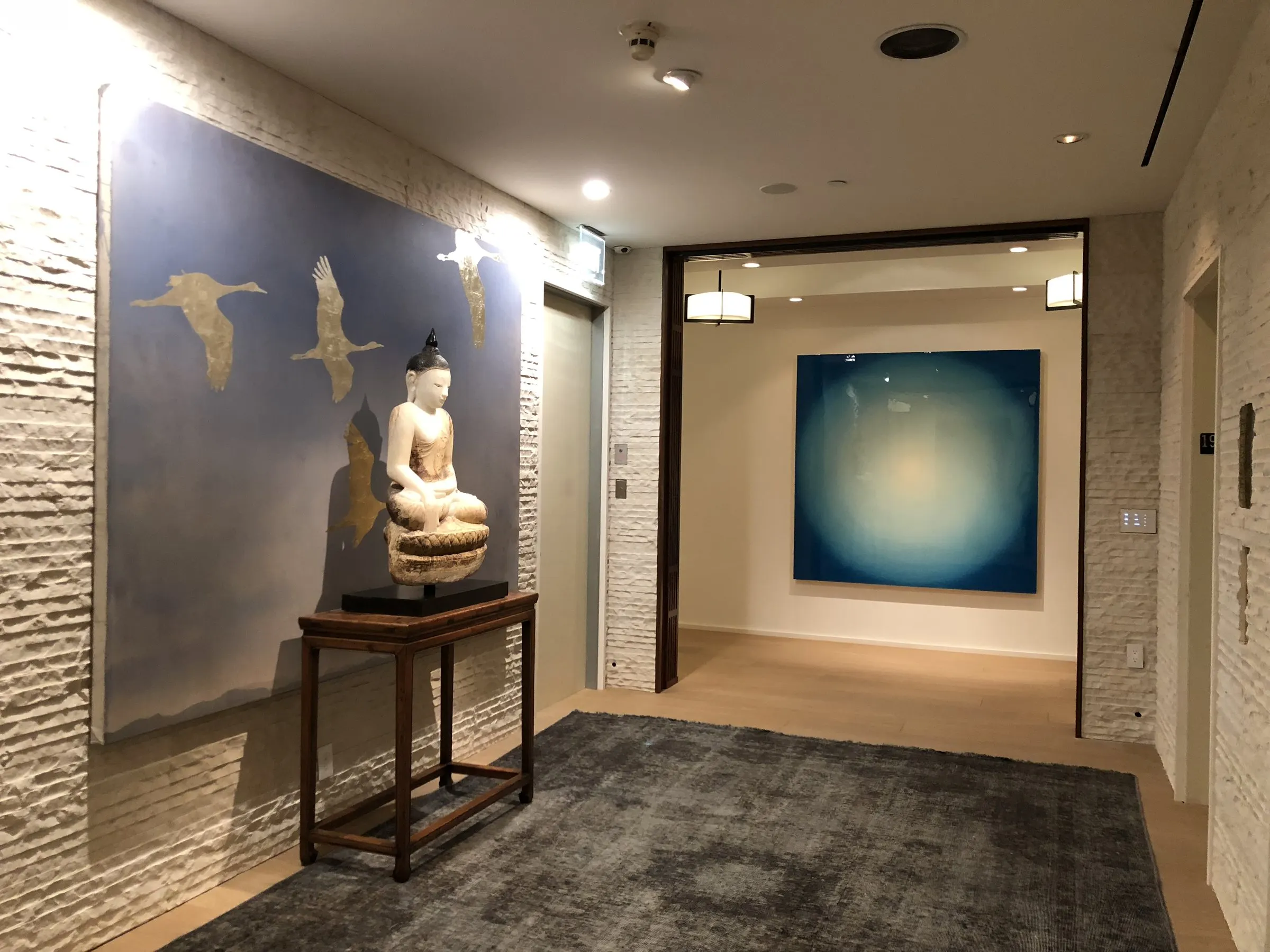 Gallery hallway with lit artwork and a sculpture on a side table