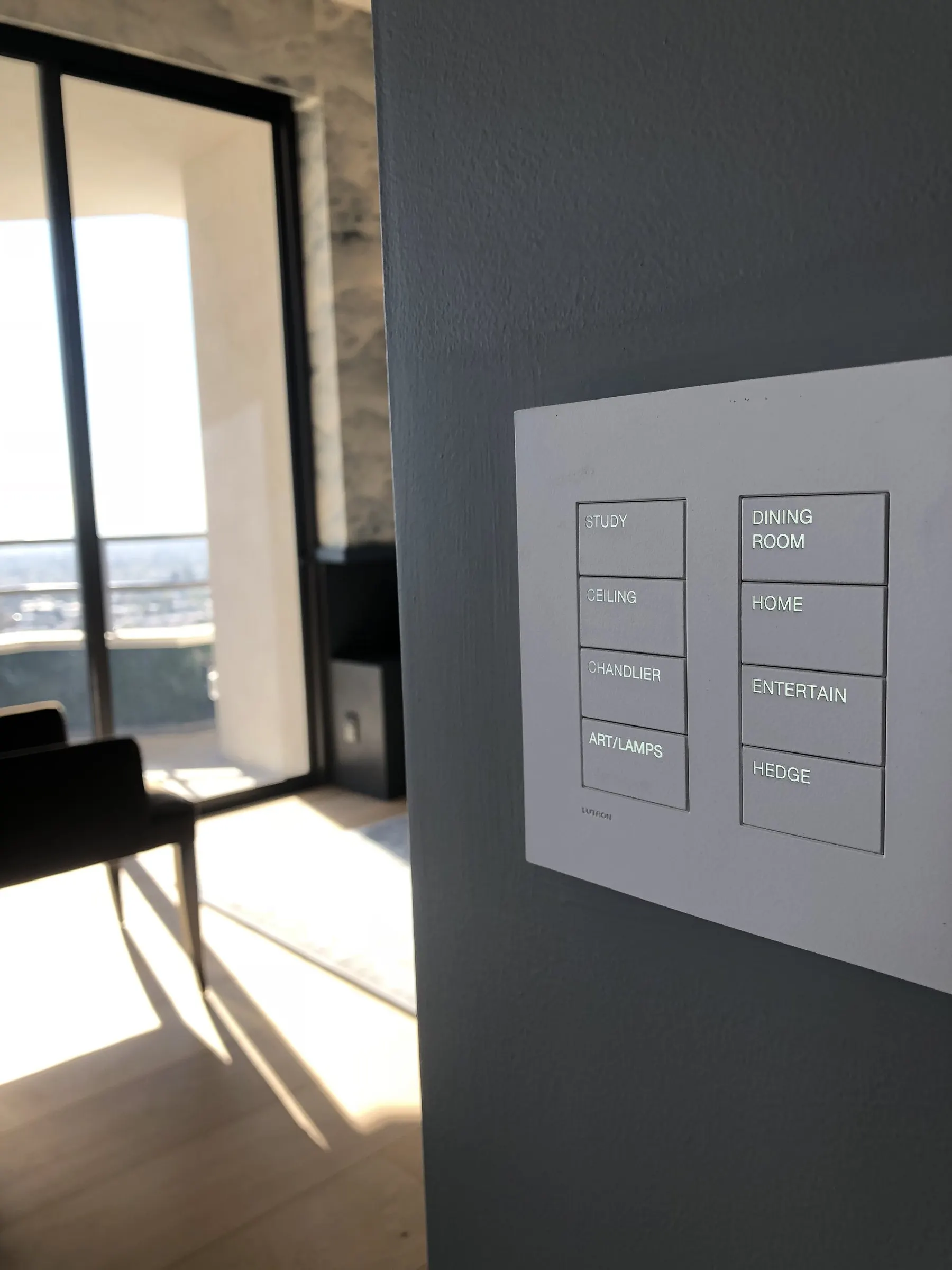 Engraved lighting keypad on a gray wall with a sunlit view room beyond