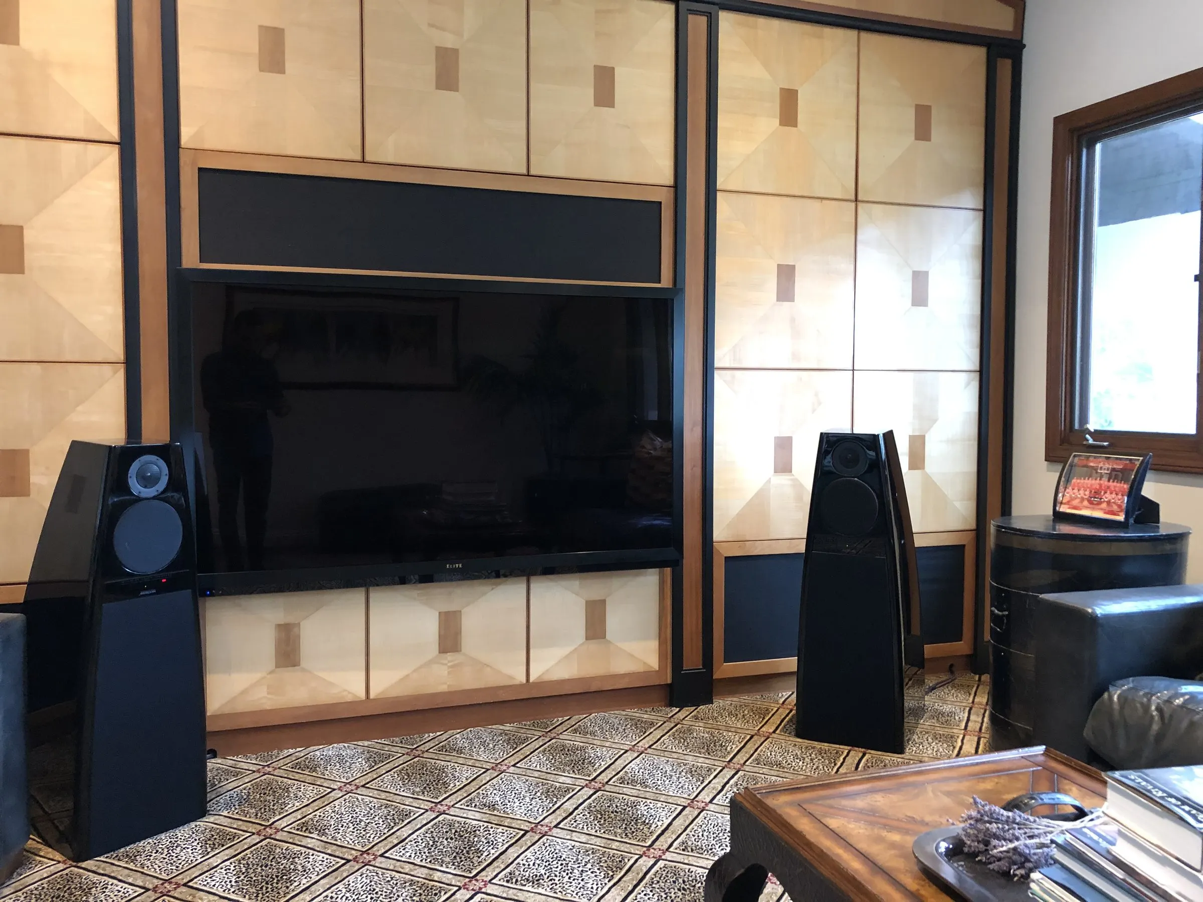 Two black tower speakers flanking a large display set into wood paneling