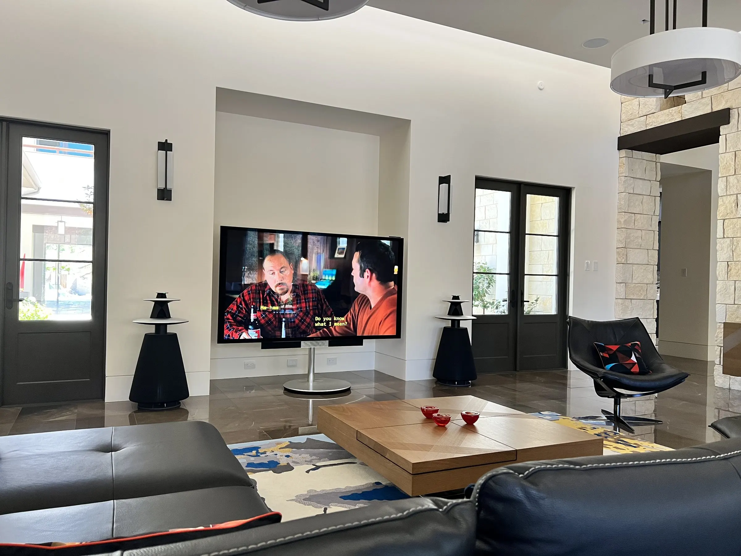 Modern living room with sculptural speakers beside a large display playing a film