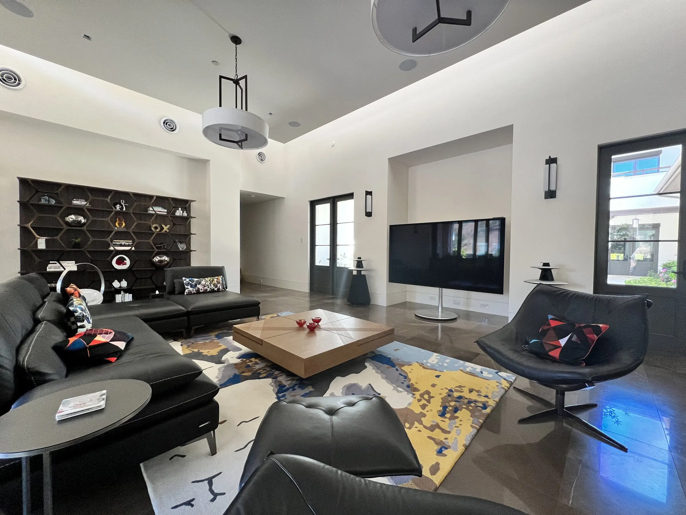 Modern living room with sculptural floor speakers beside a large display and leather lounge chairs