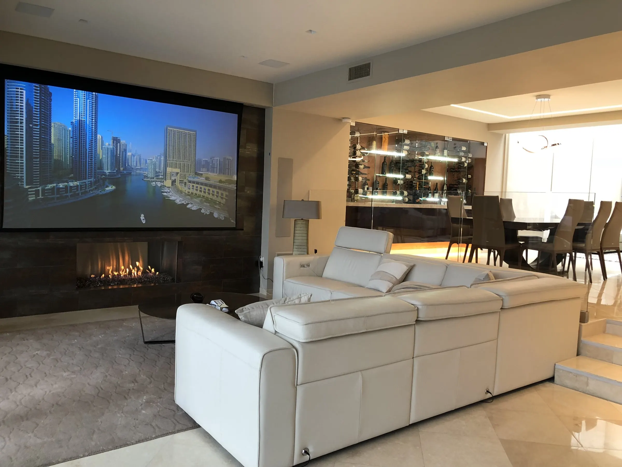 Living room with a projection screen above a fireplace, seen from beside the dining area