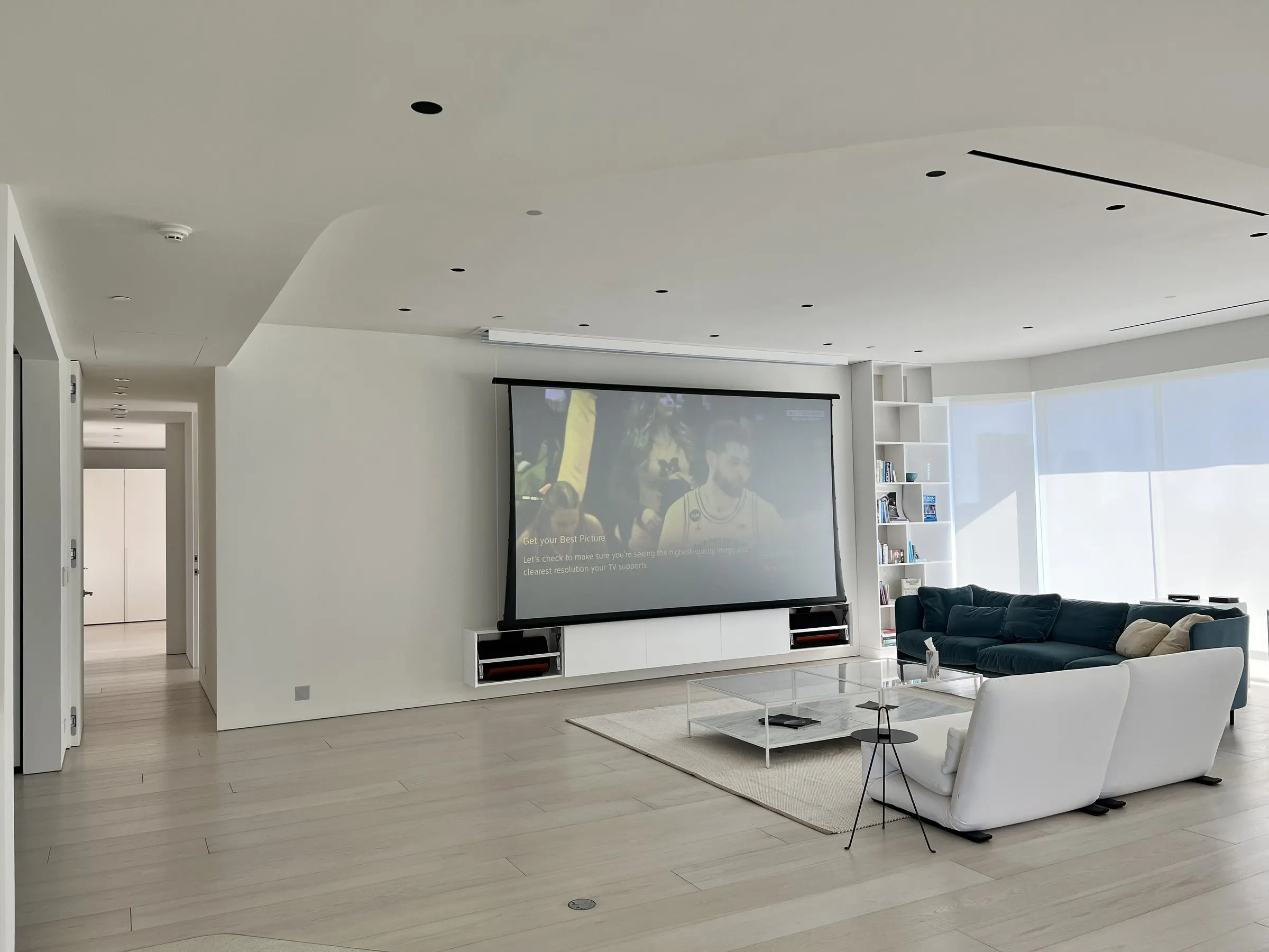 Open living room with a white sectional facing a lowered projection screen