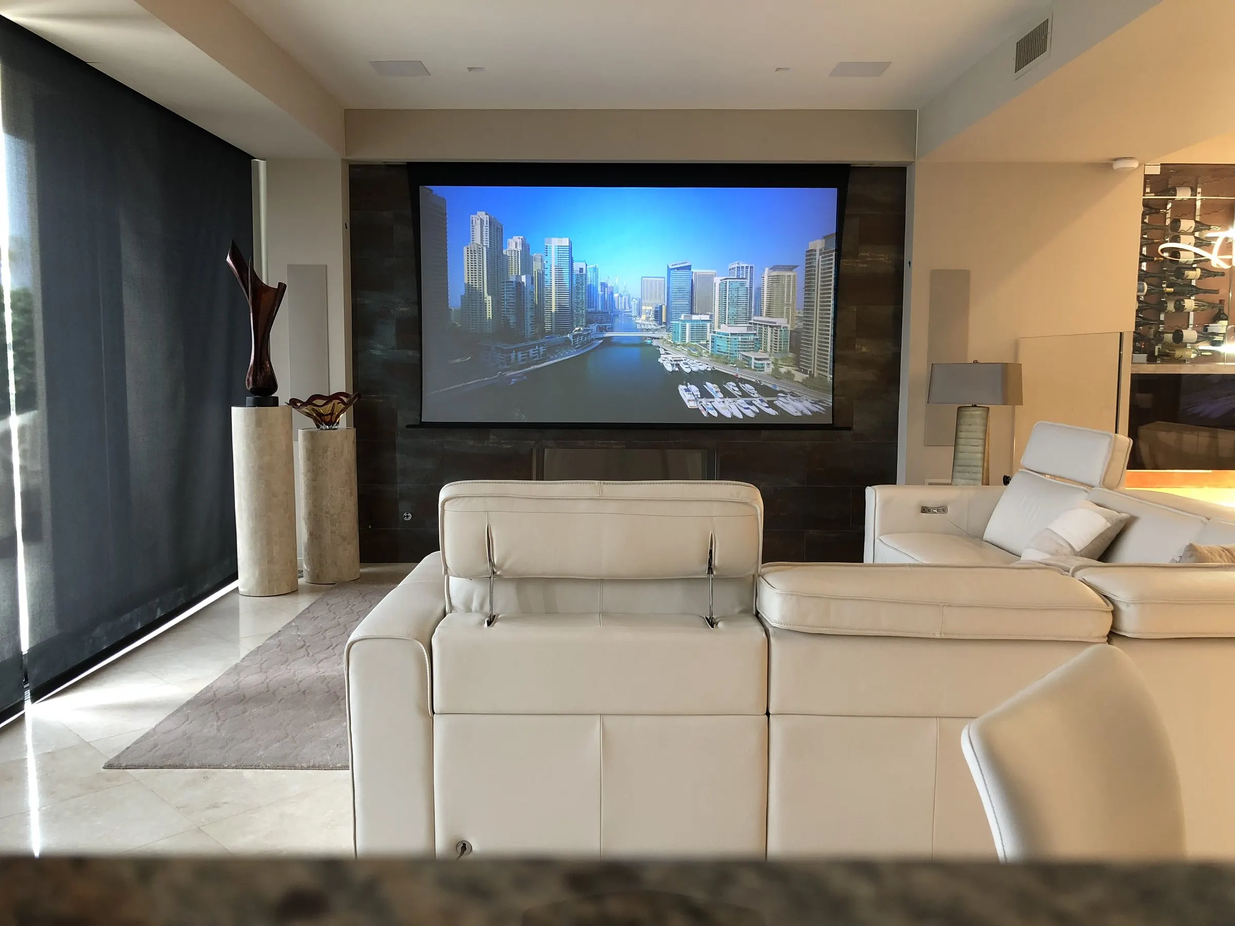 Living room with dark motorized shades lowered and a projection screen showing a city skyline