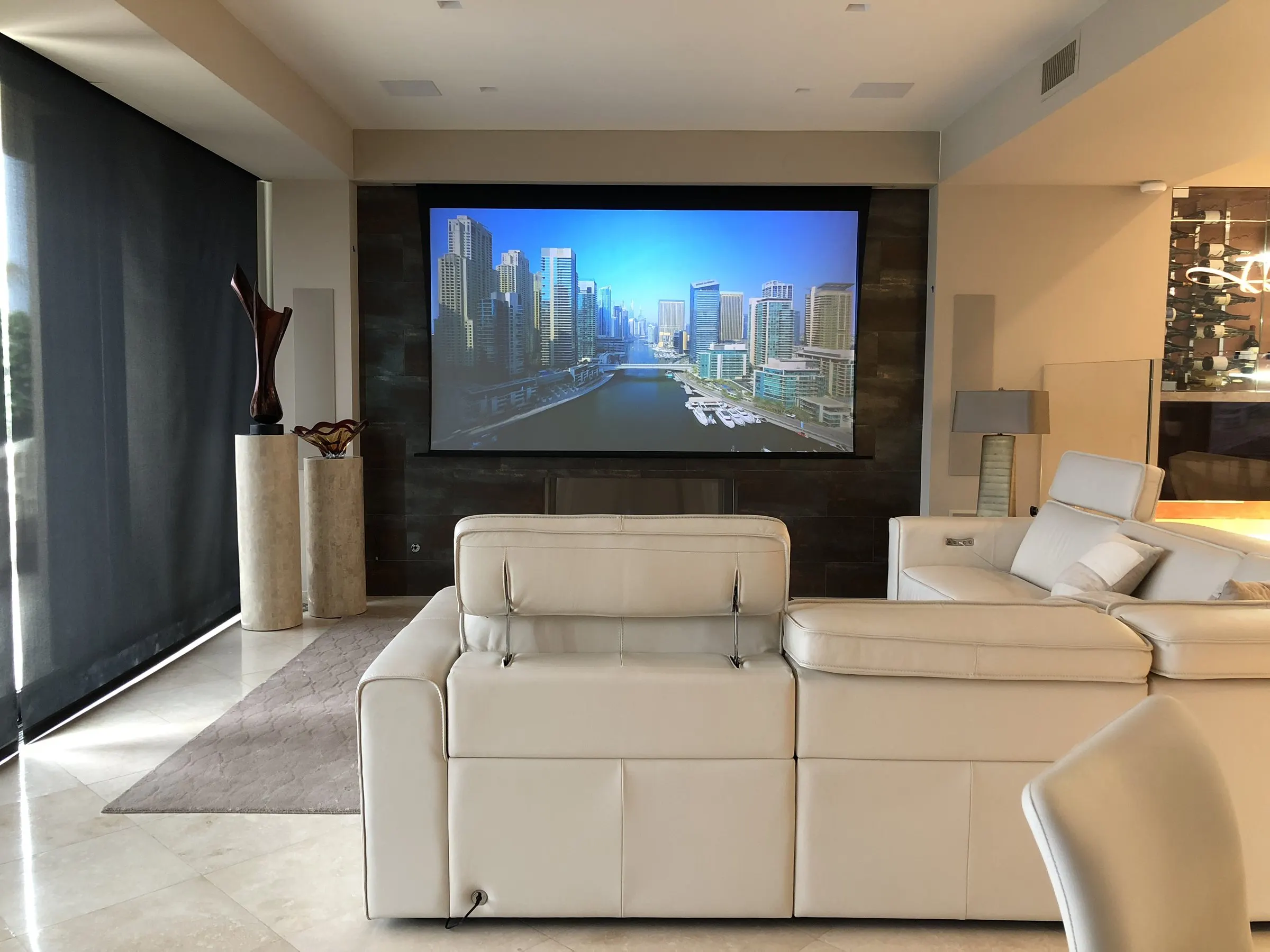 Living room with a projection screen, dark motorized shades, and a cream leather sectional