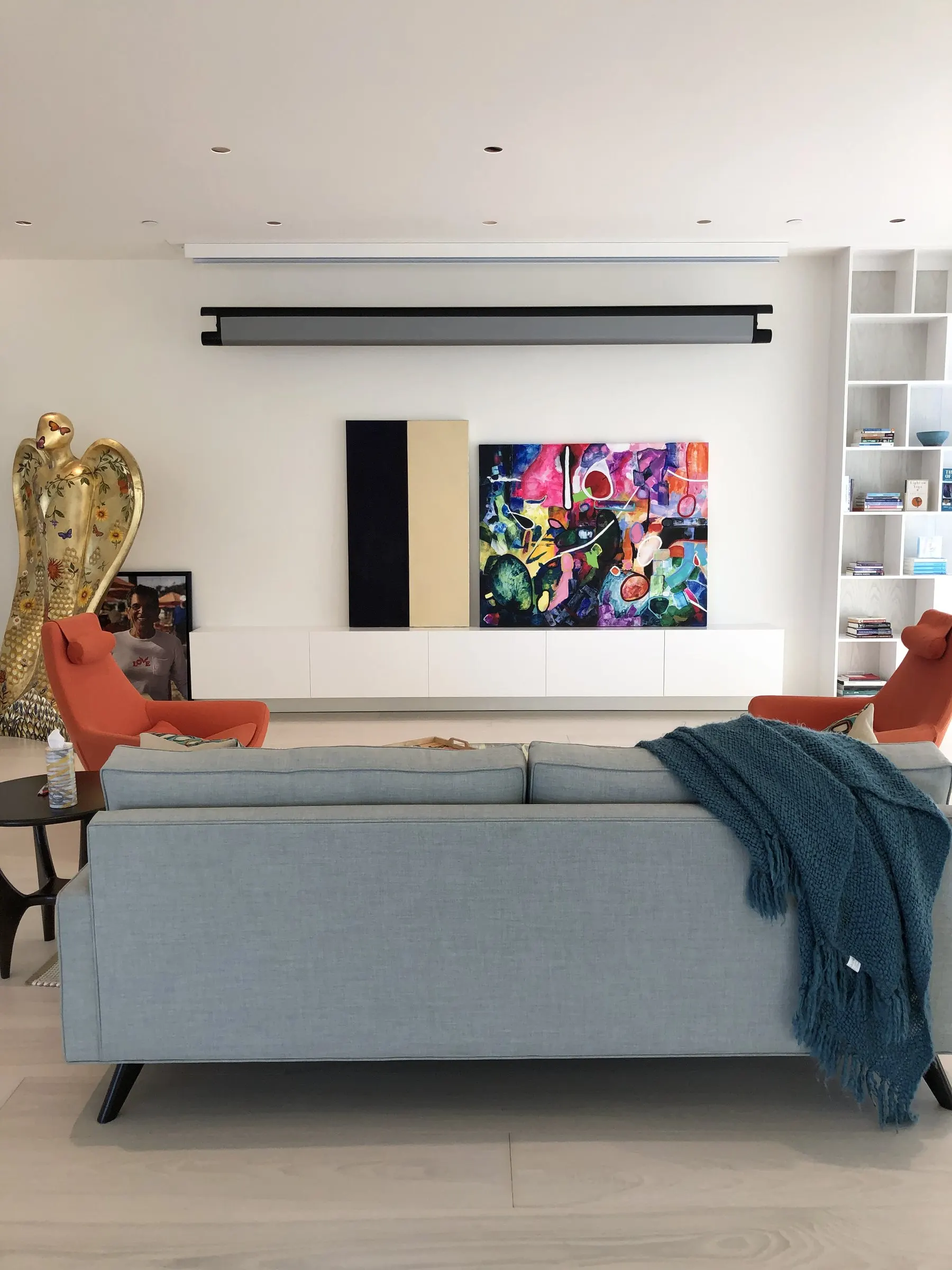 Living room with a motorized screen partway down above an art wall