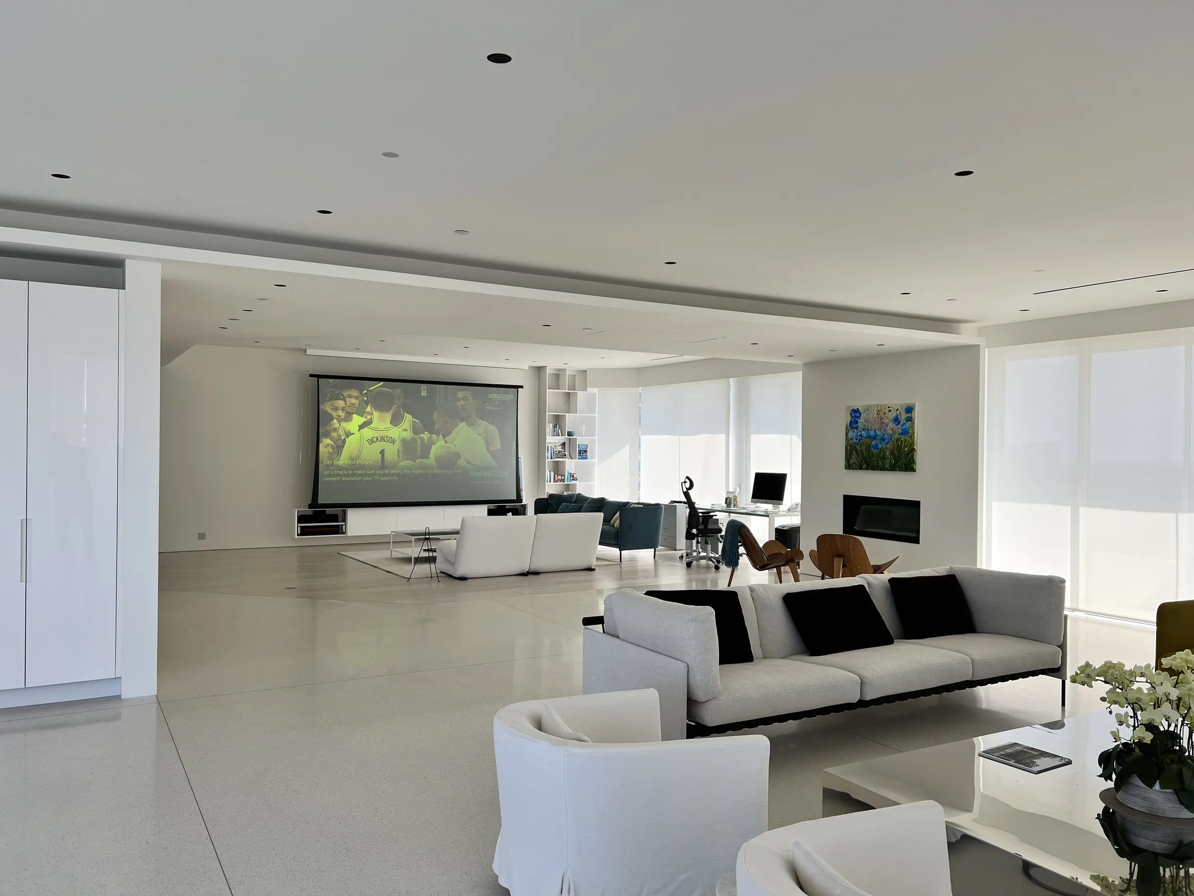 Open-plan living area with a projection screen at the far end and white shades over the windows