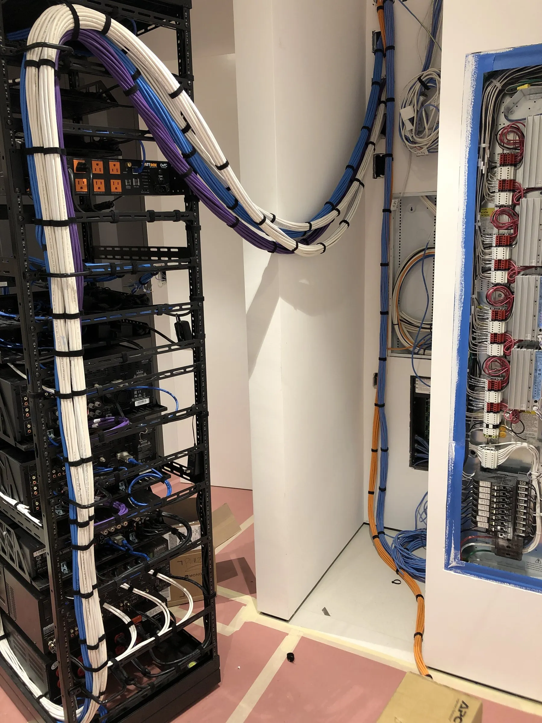 Equipment rack mid-build with bundled cabling routed into the wall beside an electrical panel