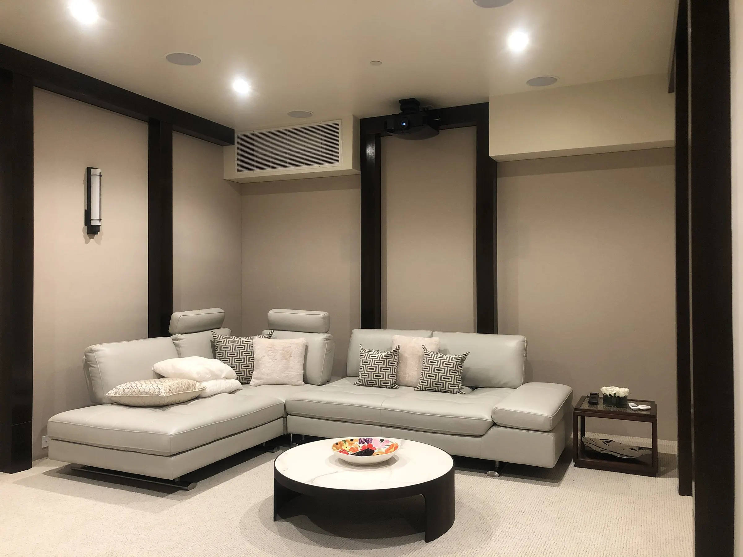 Compact theater room with a sectional sofa, ceiling-mounted projector, and wall sconces