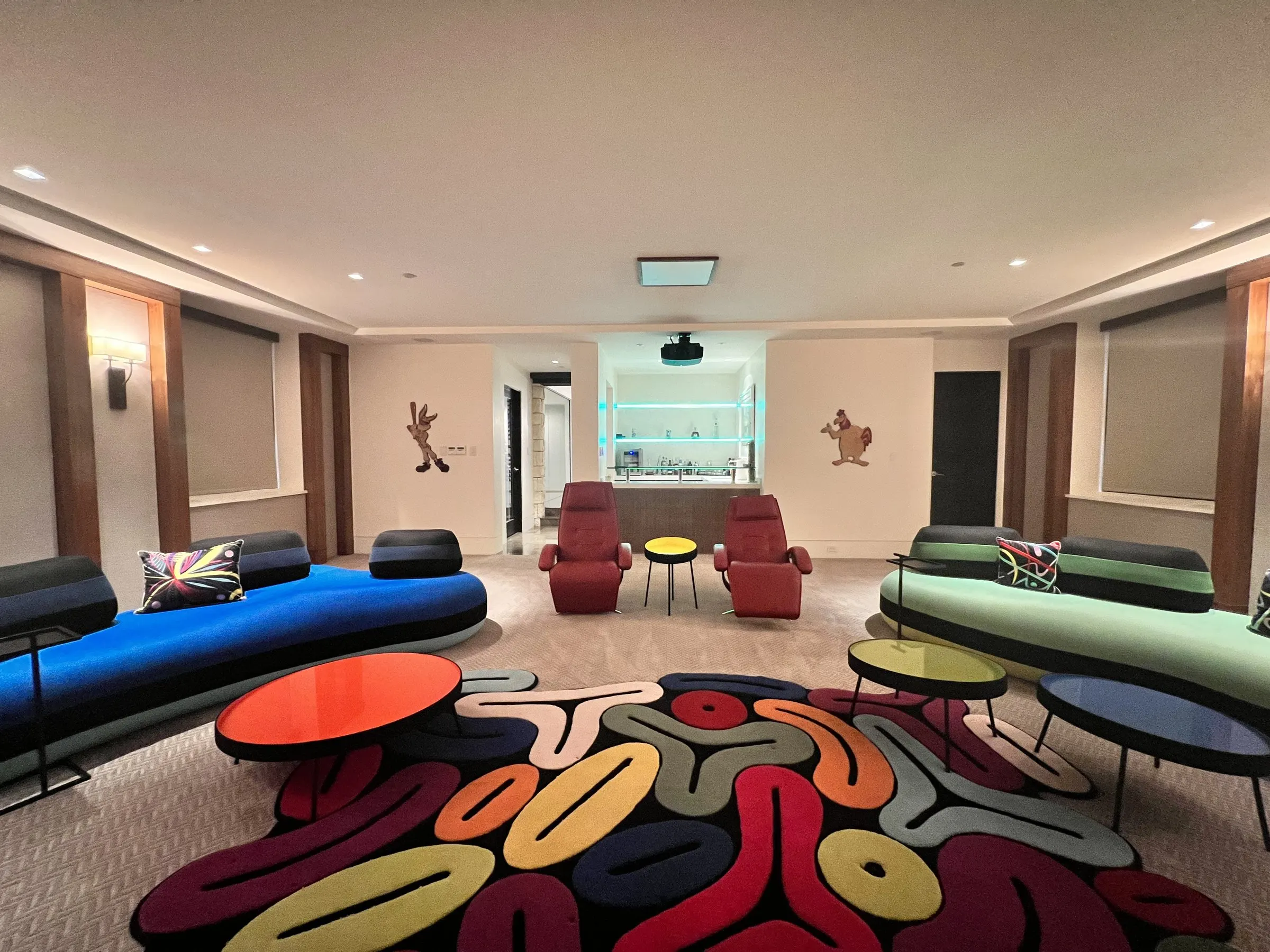 Lounge theater seen from the screen wall, looking back toward seating, rug, and a lit bar
