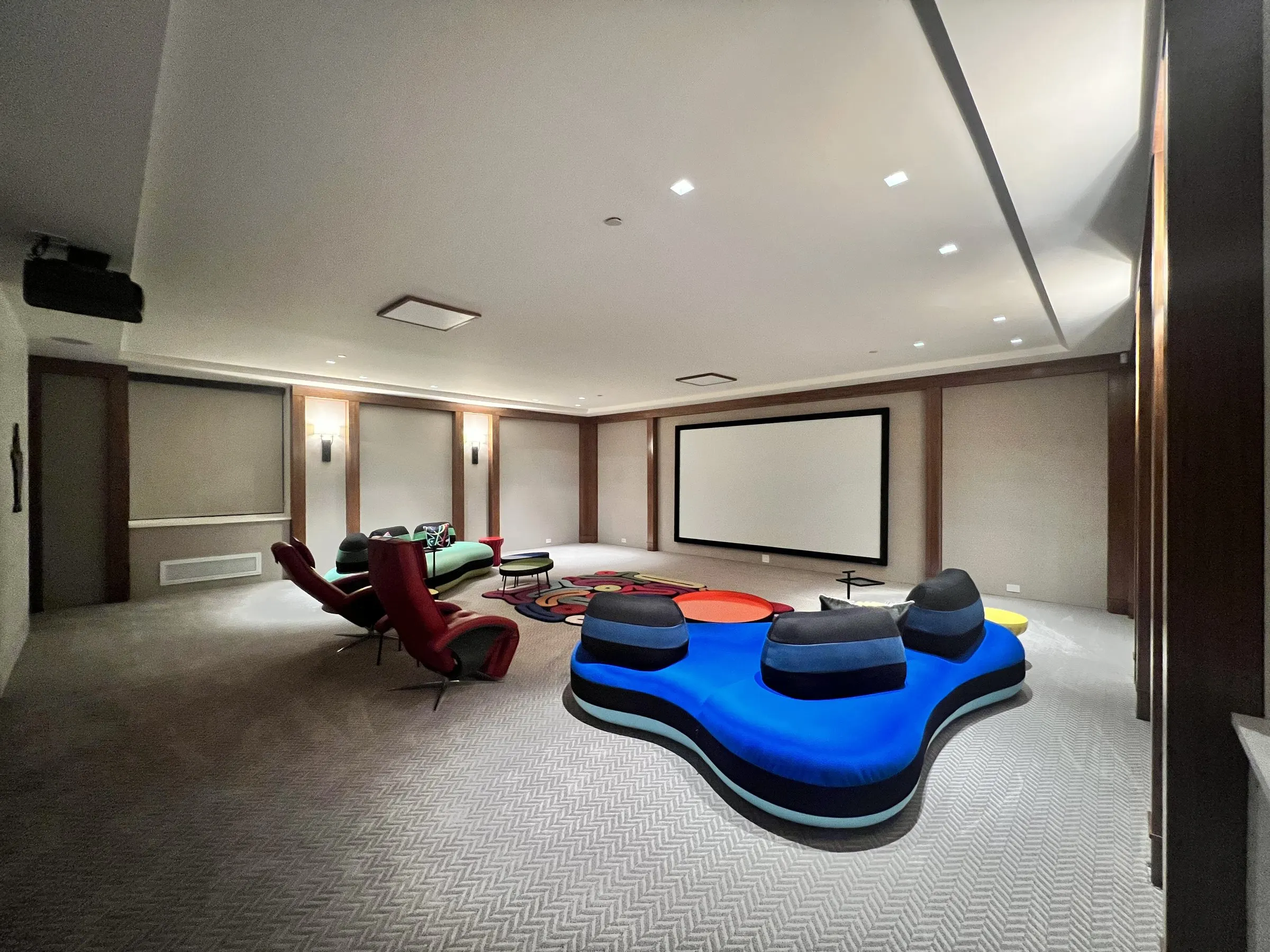 Lounge theater with blue and green sculptural sofas facing a projection screen, projector mounted on the ceiling