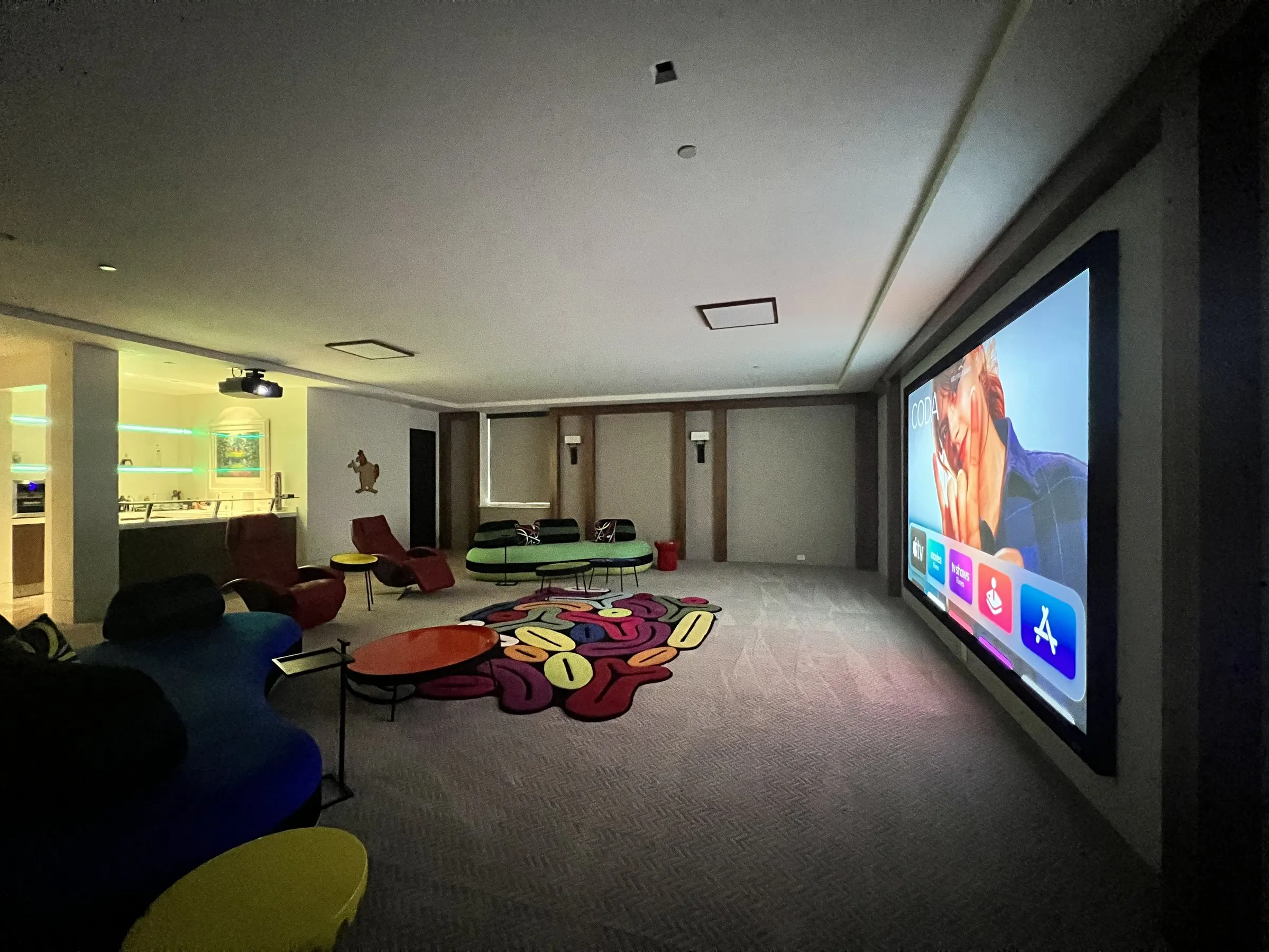Lounge theater viewed from the side with a large illuminated projection screen on the right wall