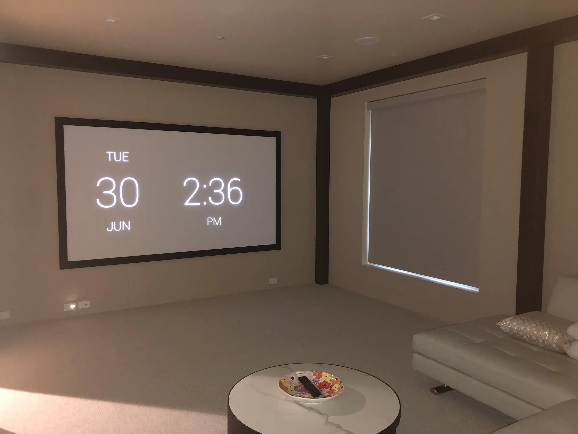 Compact theater with a projection screen, a lowered blackout shade, and a white leather sectional