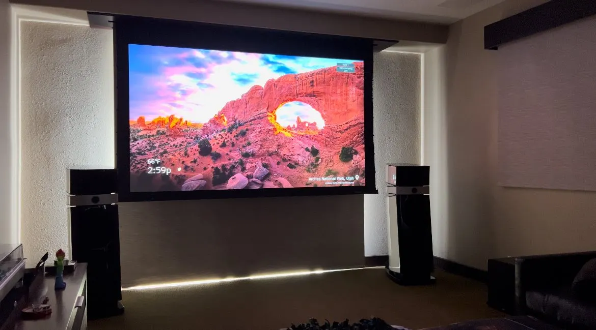 Projection screen lowered between tall tower speakers with a lit floor reveal below