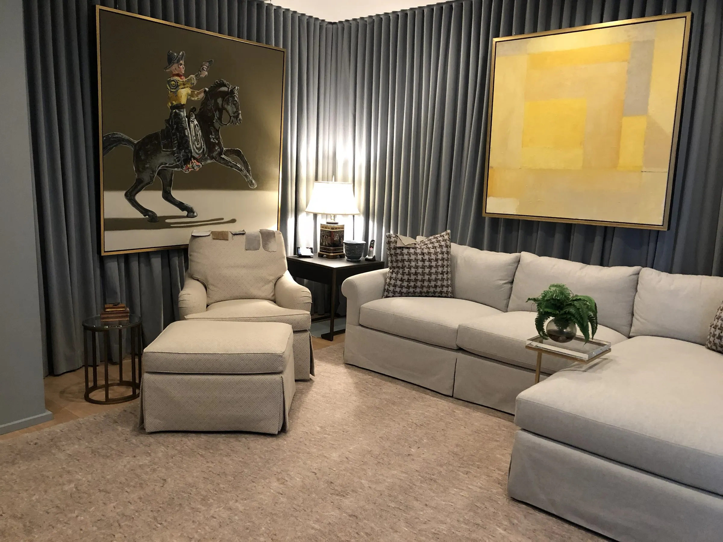 Sitting room with gray drapes, large paintings, and a sectional sofa
