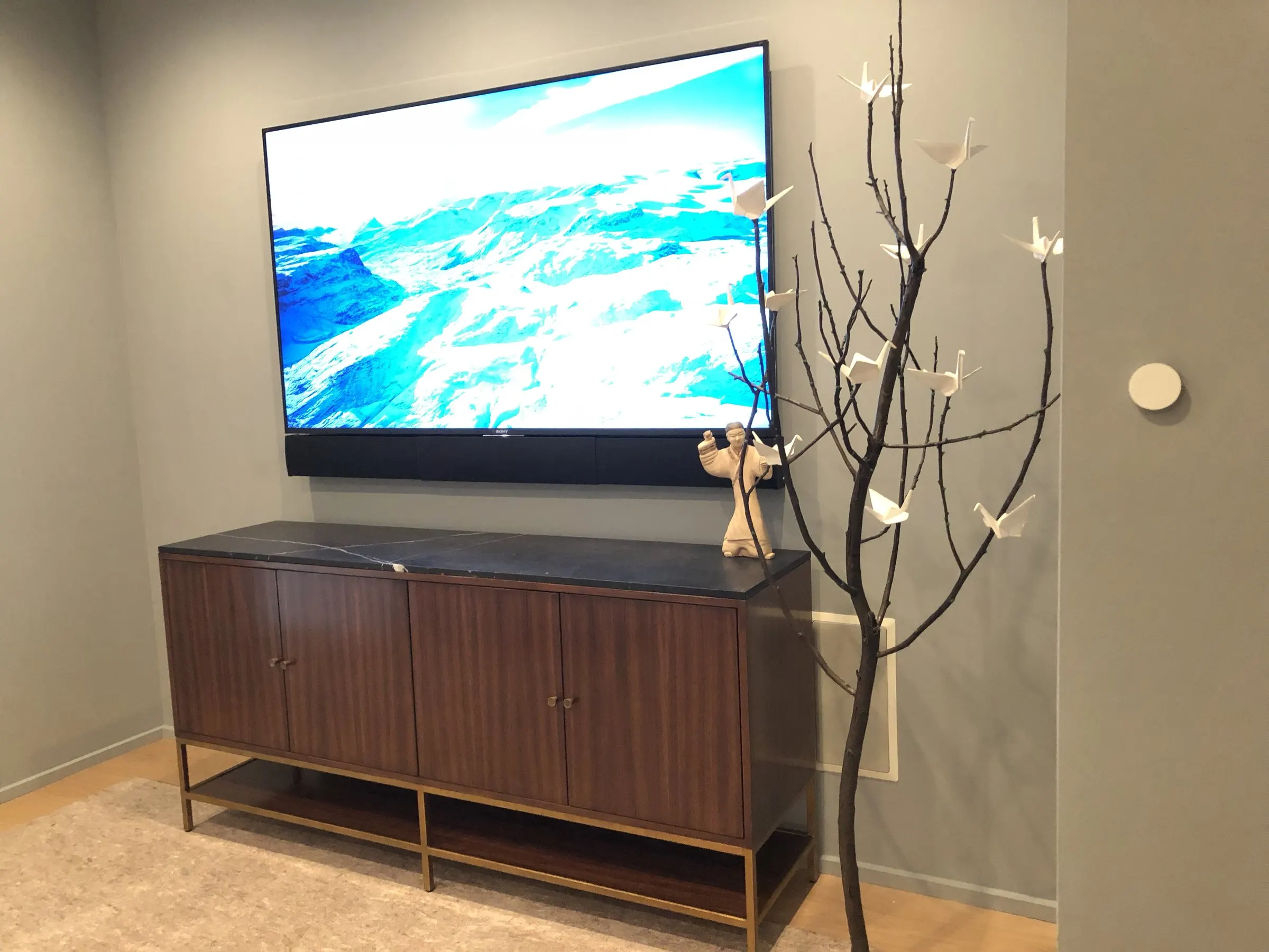 Wall-mounted television above a walnut credenza with a decorative branch