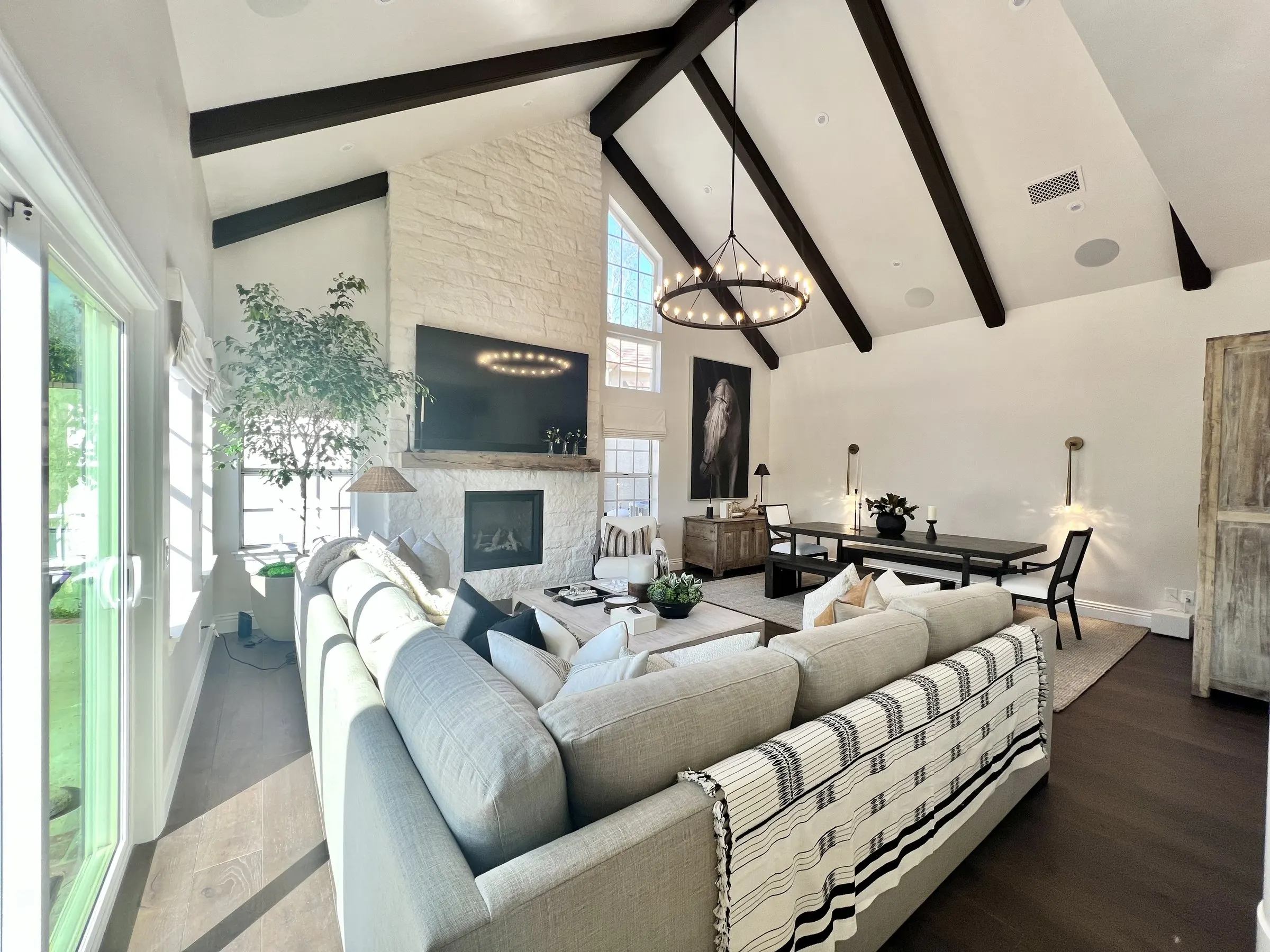 Vaulted living room with dark beams, a television above the stone fireplace, and discreet in-ceiling speakers