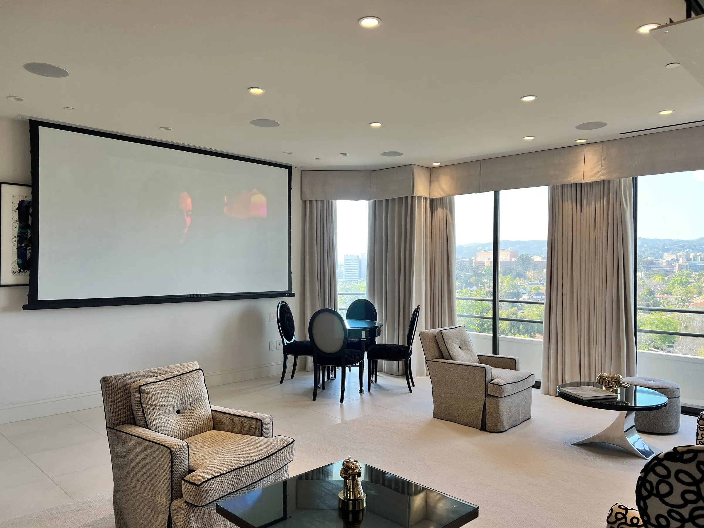 High-rise living room with floor-to-ceiling windows and a large projection screen lowered on the side wall